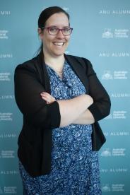 Deanne Allan smiling at the camera as she stand arms crossed in-front of a light-blue backdrop