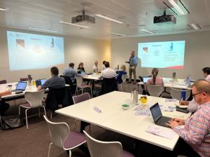 Around 15 AustraliaGovernment officials sit at desks, watching the course facilitator present